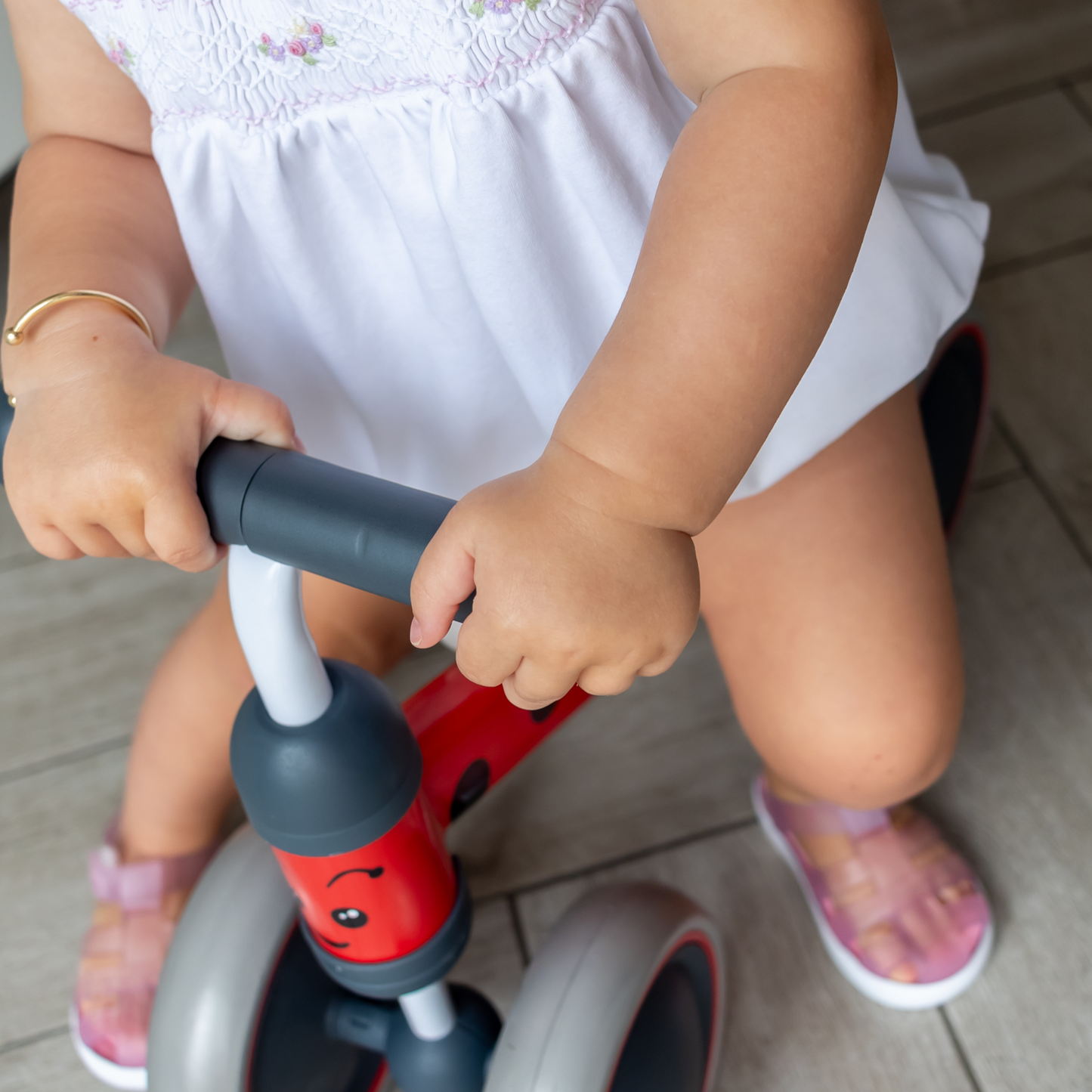 Child's hands on a red and gray balance bike with a white background