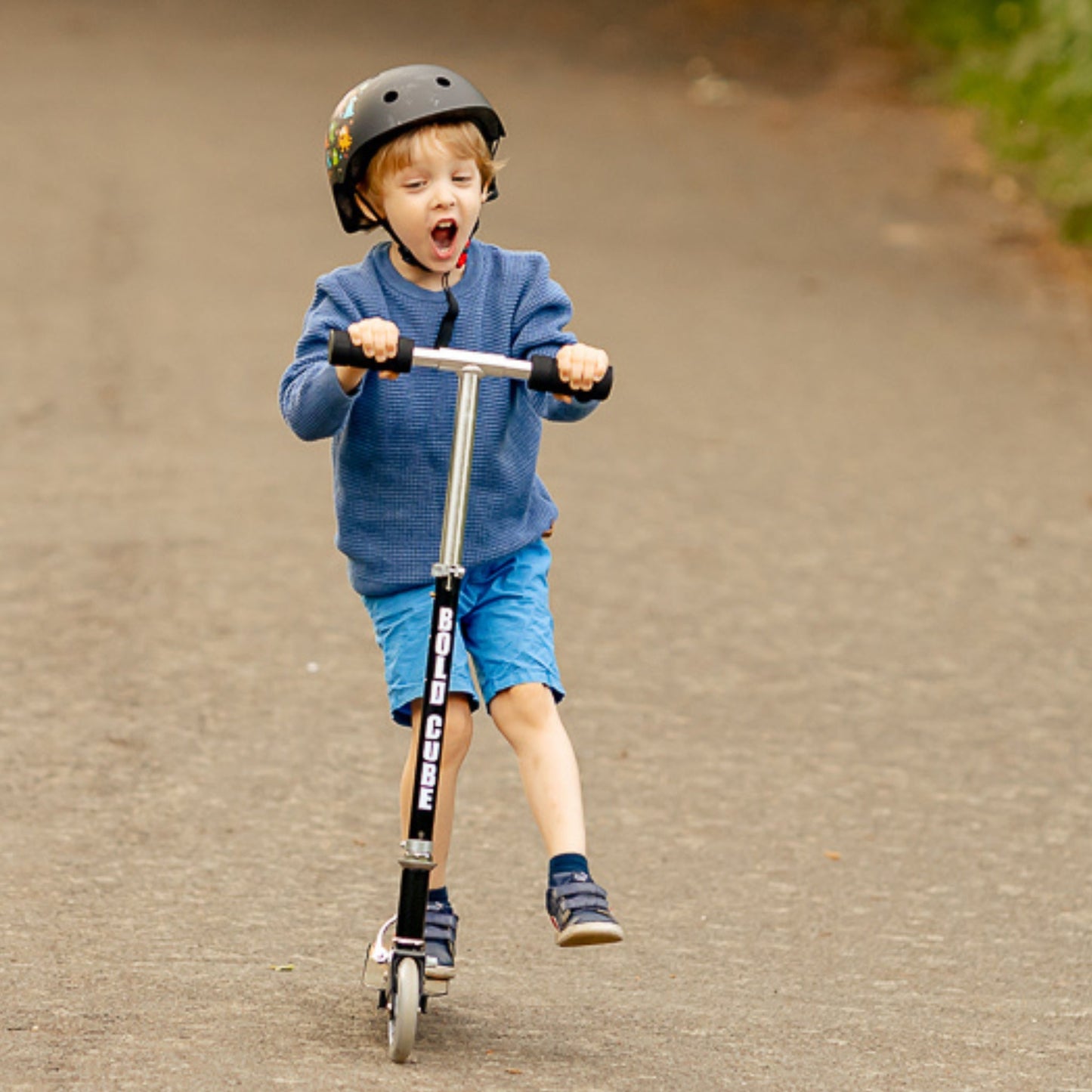 Child riding a scooter on a paved road wearing a helmet
