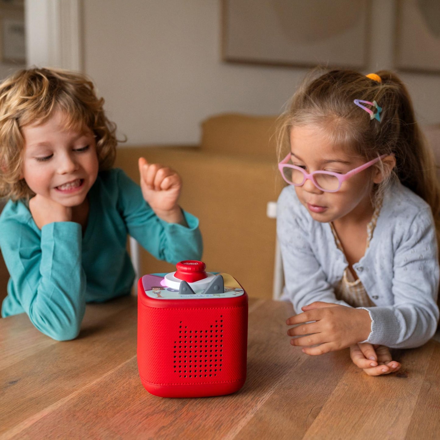 Two children playing with a red toy on a wooden table.