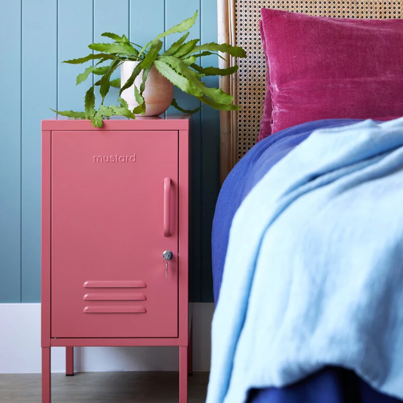 Pink metal cabinet with a plant next to a bed with pink pillow and blue blanket.