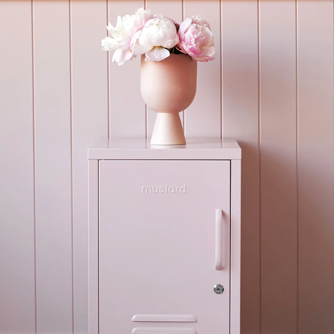 Pink cabinet with a vase of flowers against a wooden wall