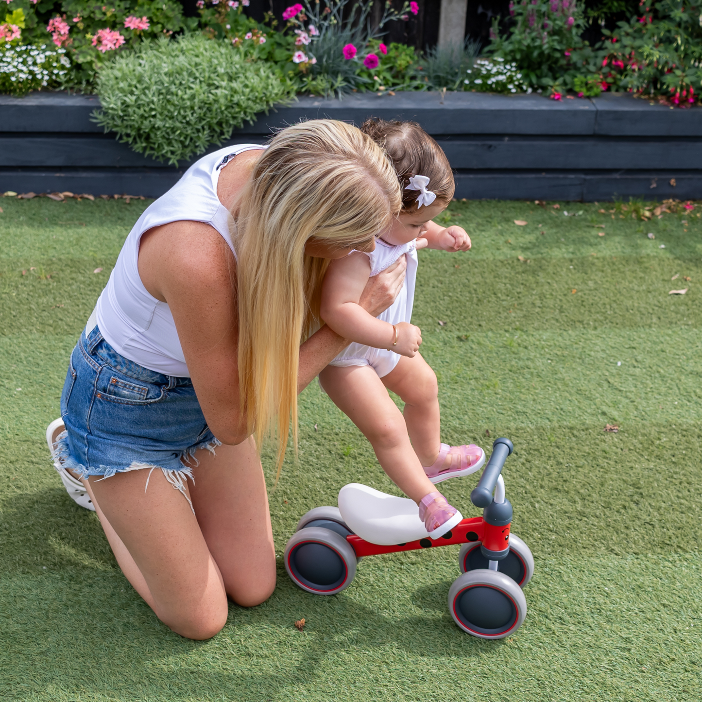 Woman teaching a child on a tricycle in a garden setting