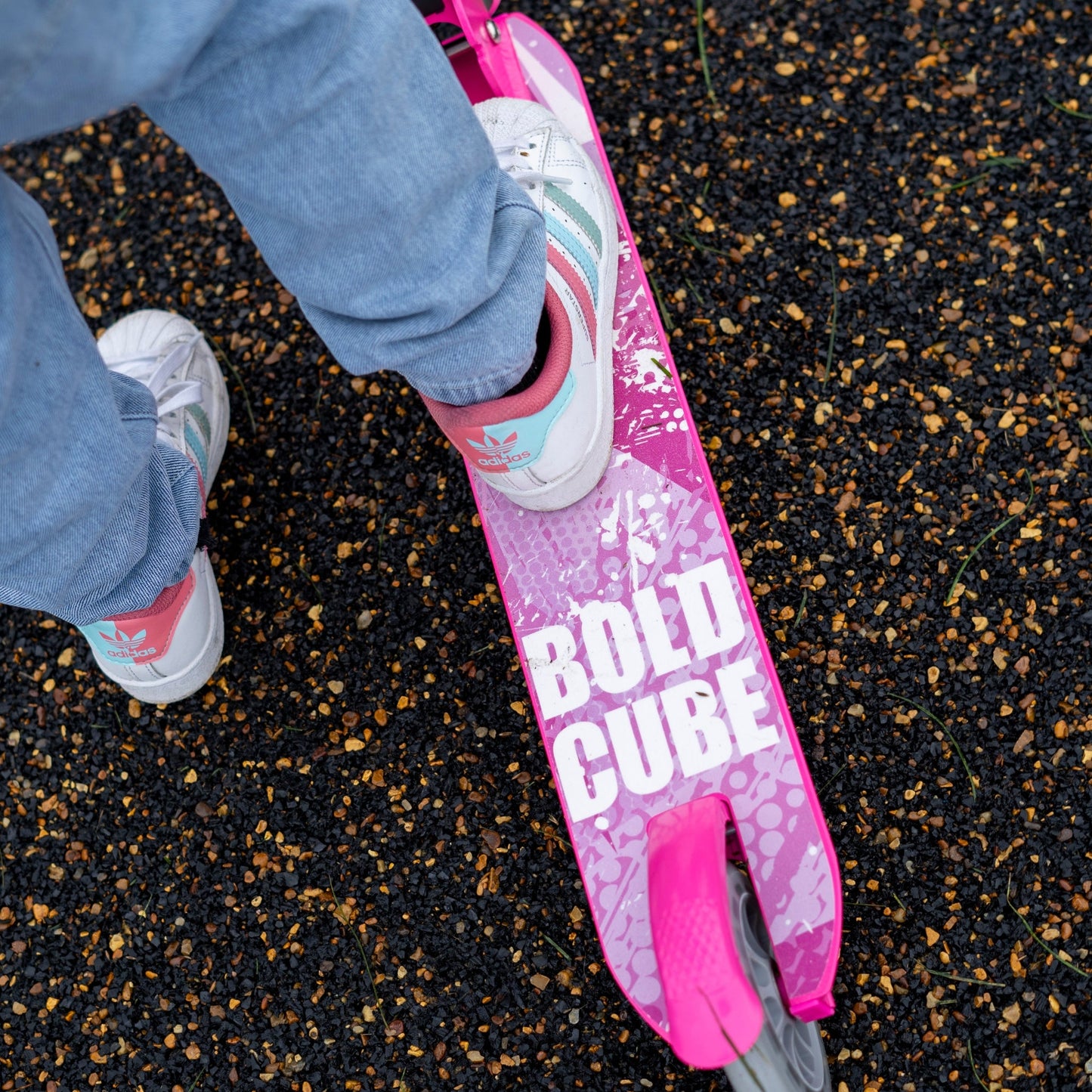 Person wearing blue jeans and white sneakers with pink accents standing on a pink skateboard with 'BOLD CUBE' text.