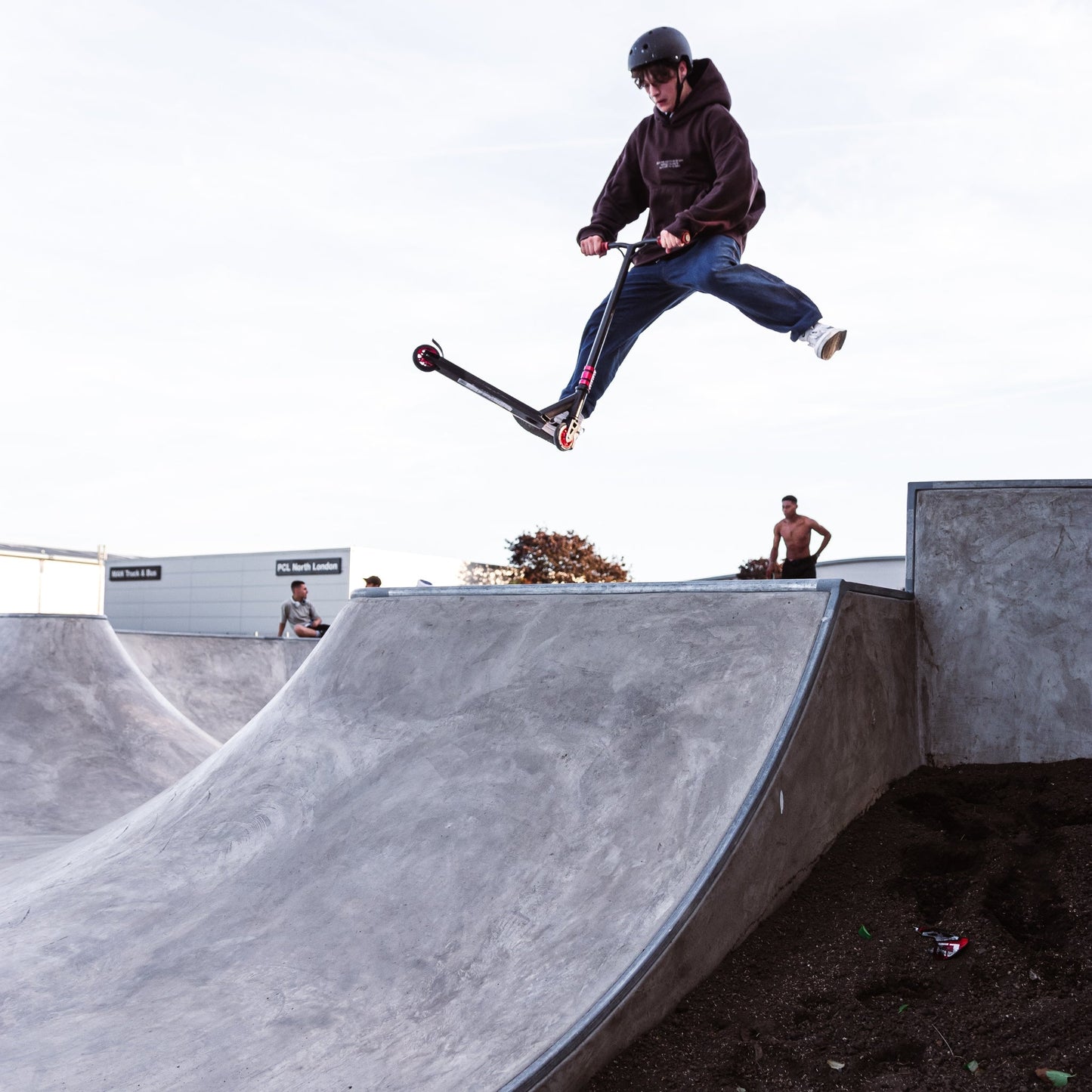 Person riding a scooter in mid-air over a concrete ramp at a skate park.