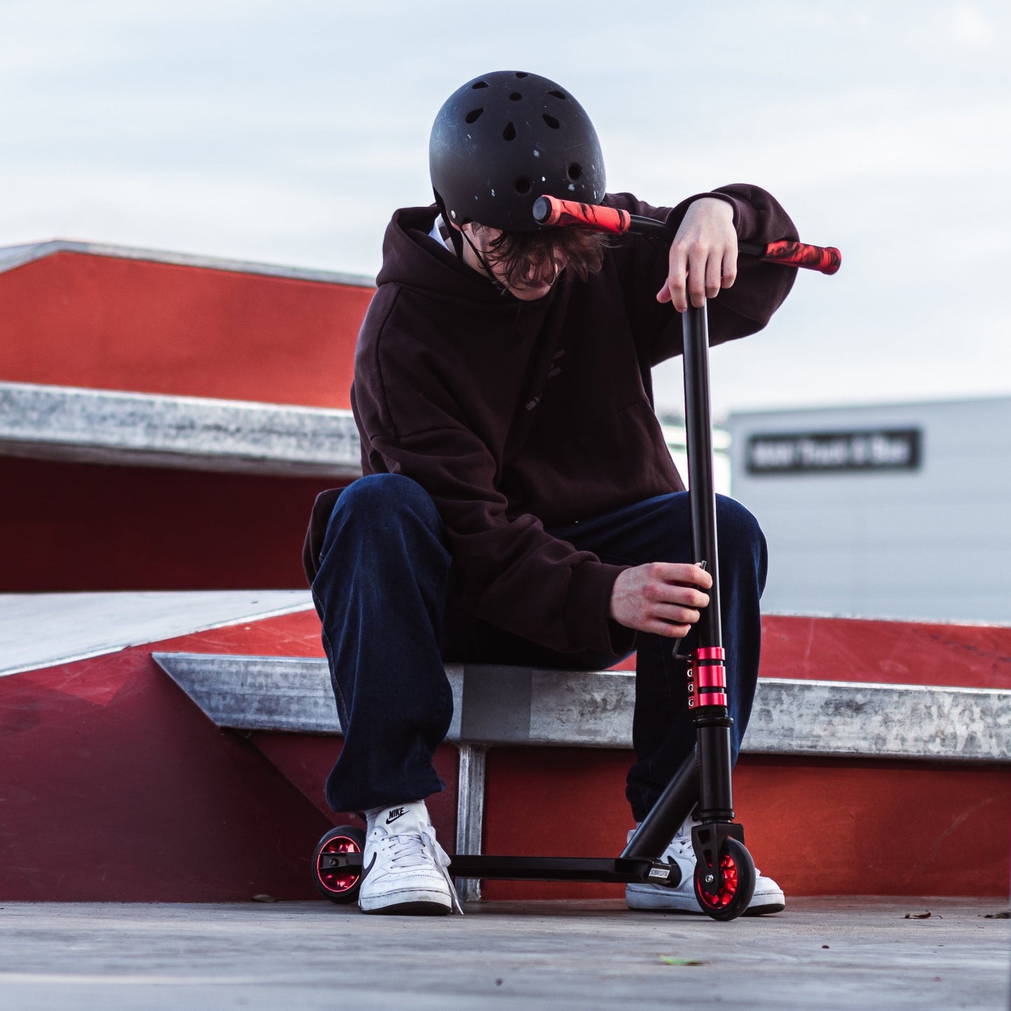 Person sitting on a red and white wall with a scooter, wearing a helmet.