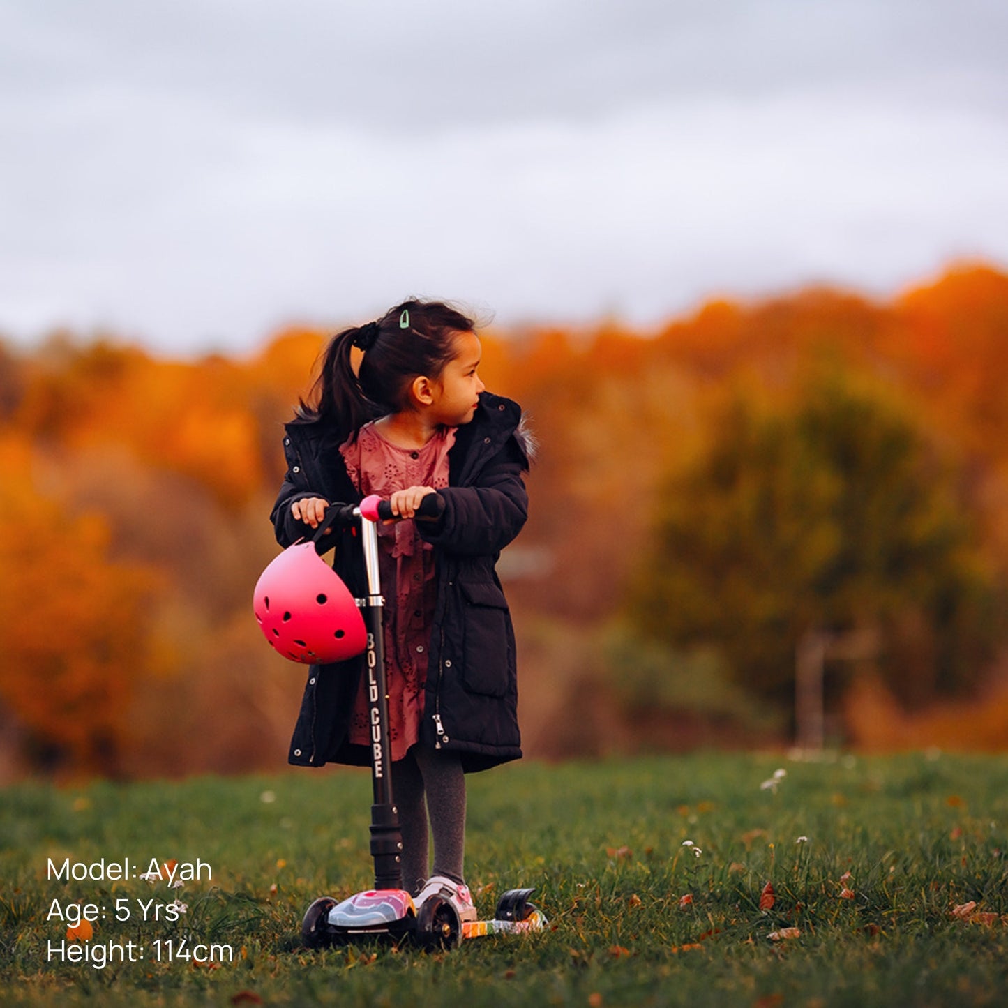 Child with a scooter and helmet in an outdoor setting with trees in the background