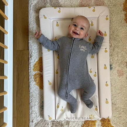 Baby lying on a soft mat with a wooden play gym in the background