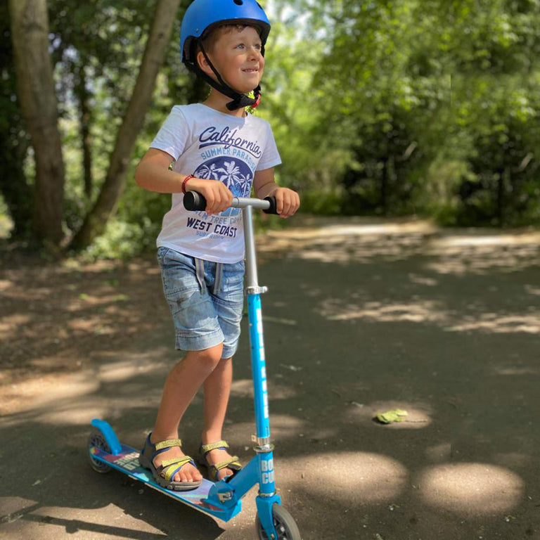 Child riding a blue scooter in a park with trees in the background