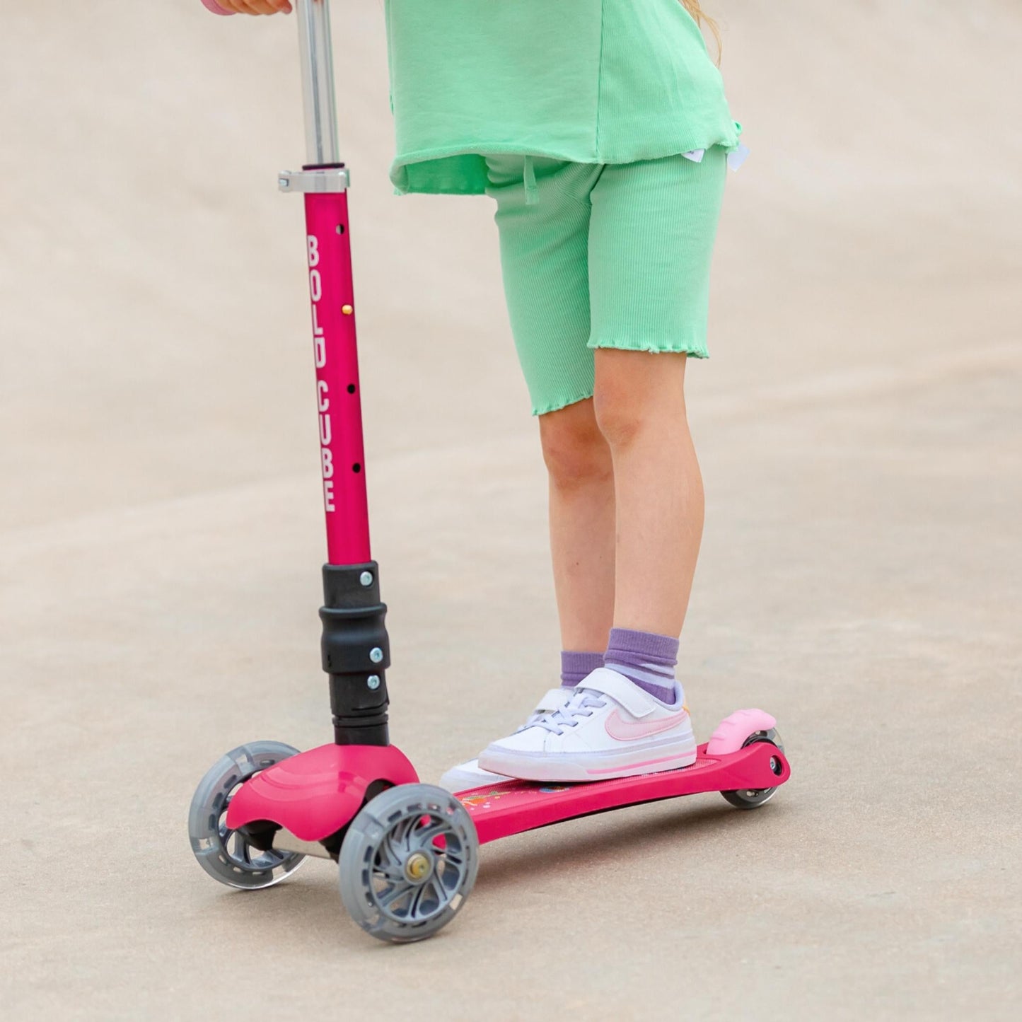 Child riding a pink scooter with a beige background