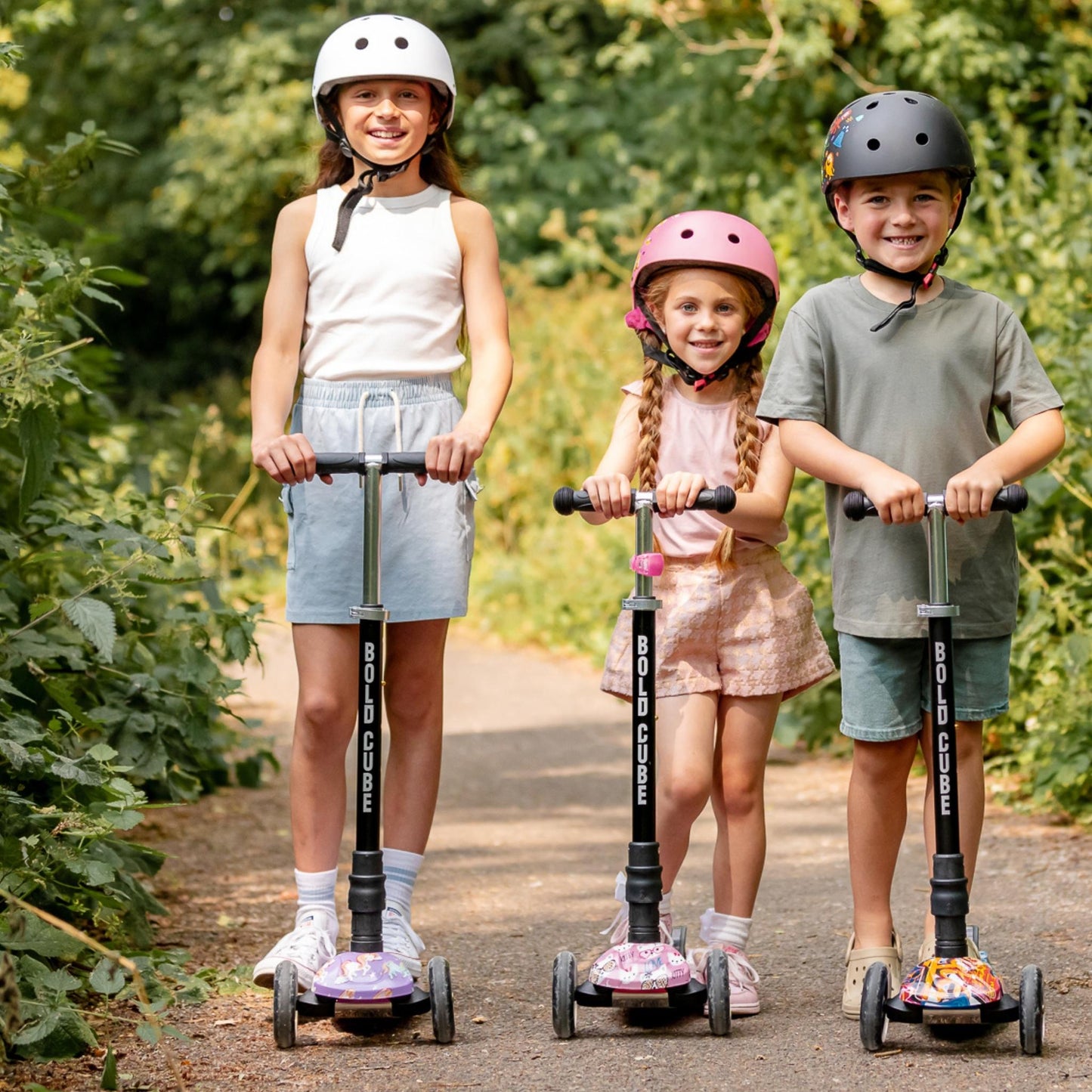 Three children on scooters wearing helmets in a park setting