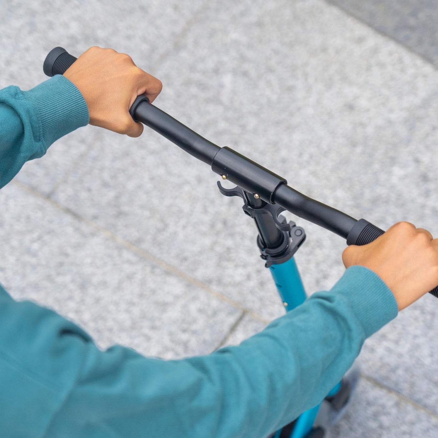 Person holding the handlebar of a blue scooter on a tiled floor.