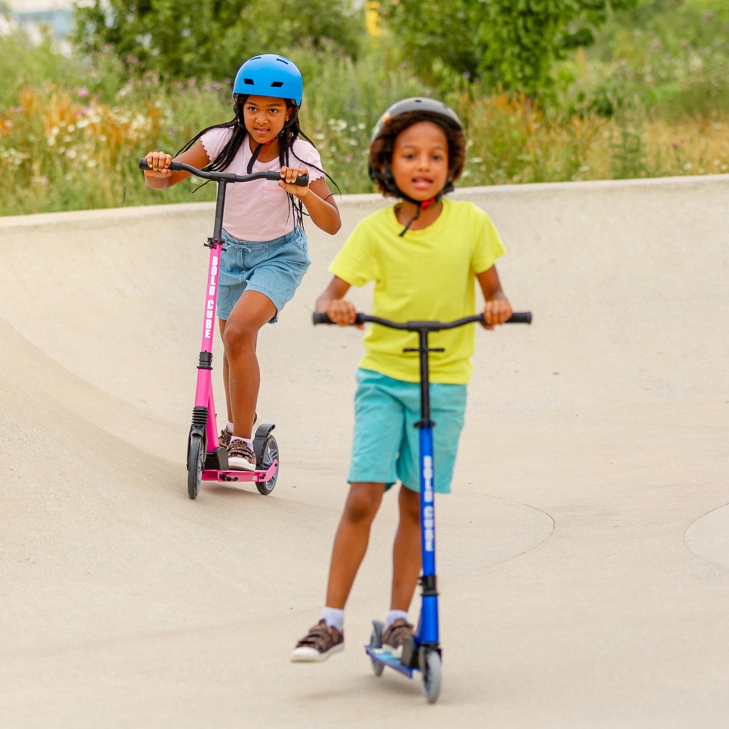 Two children riding scooters on a paved path with a natural background