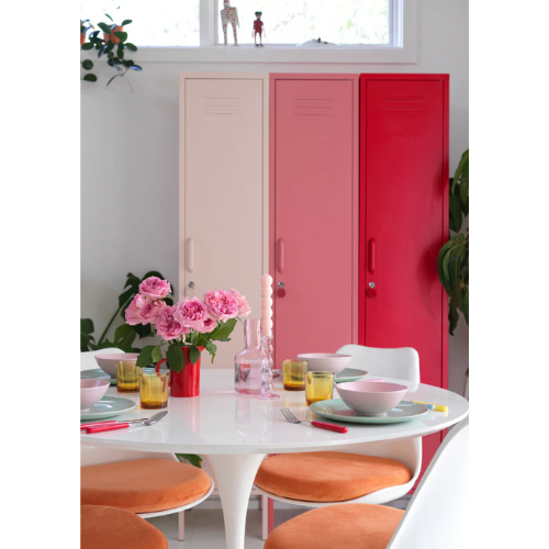 Dining area with a table set for a meal, pink flowers, and a red cabinet.