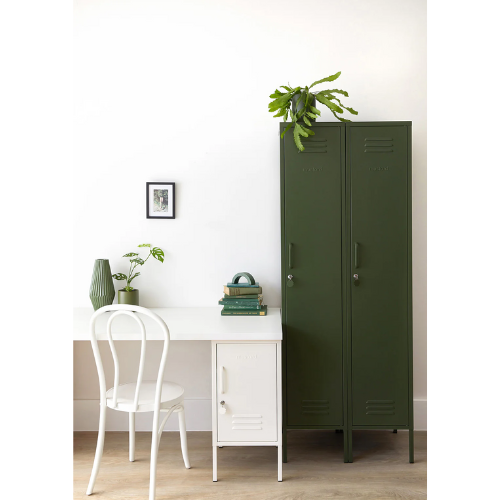 Green metal locker next to a white desk with a chair and plants in a room.