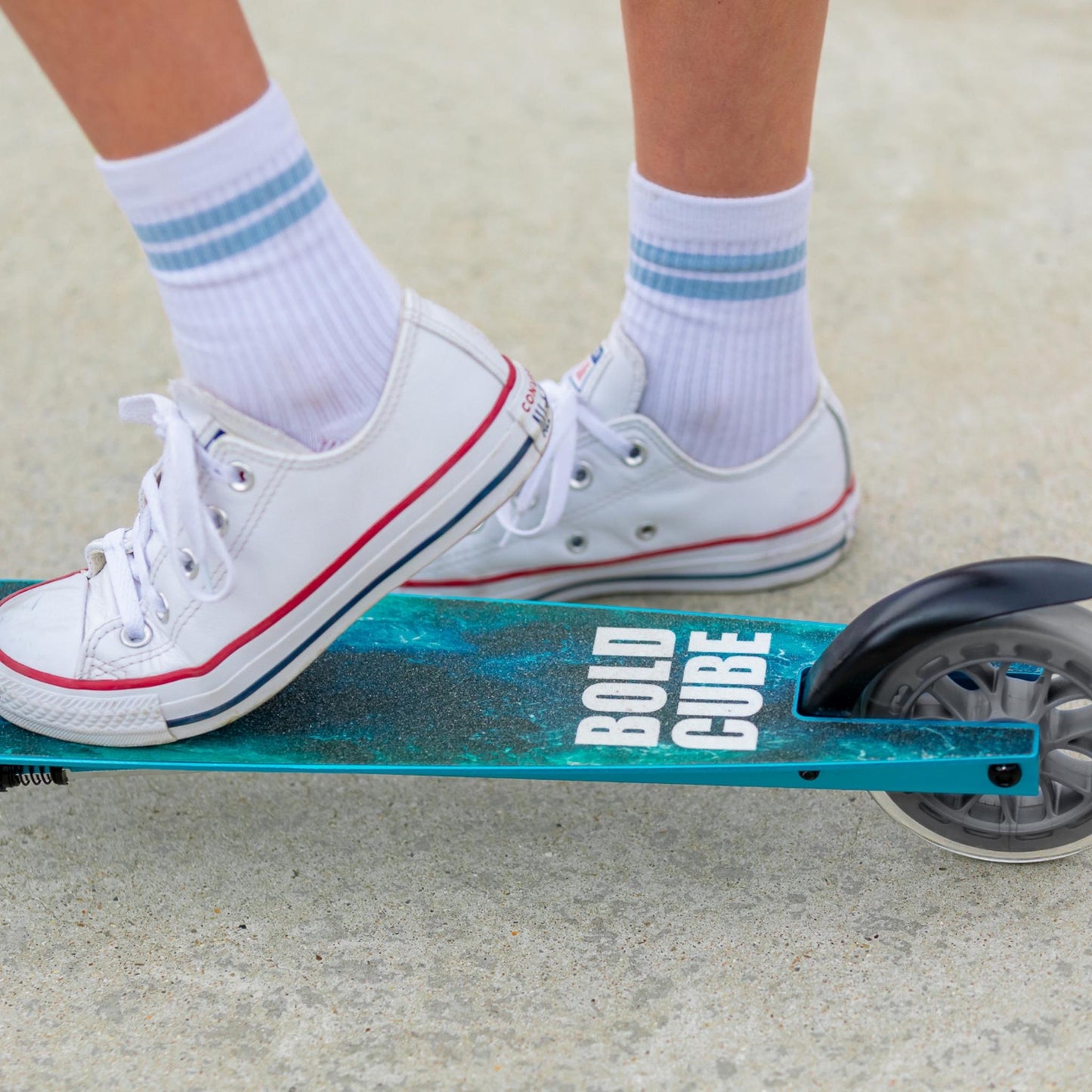 Person wearing white sneakers with red accents on a teal scooter with 'Bold Cube' branding.