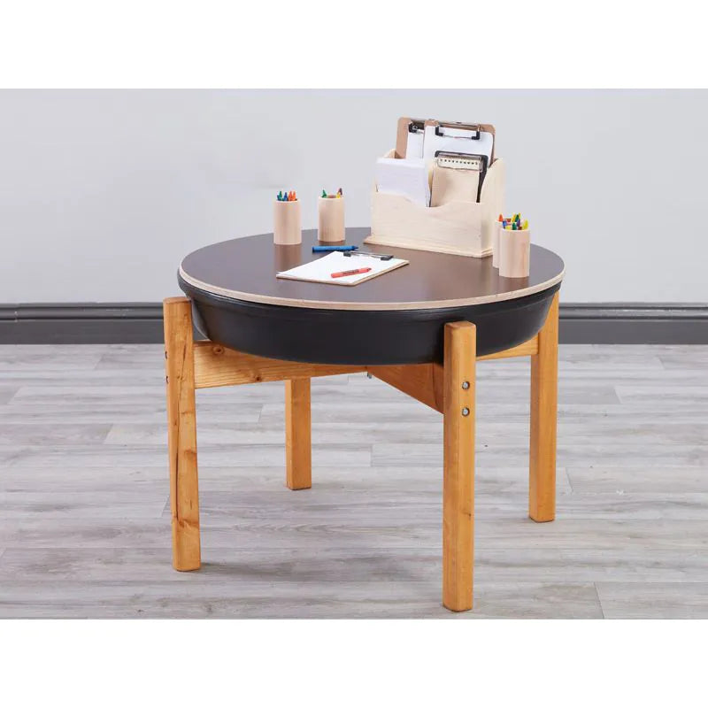 Round table with black top and wooden legs on a gray floor.