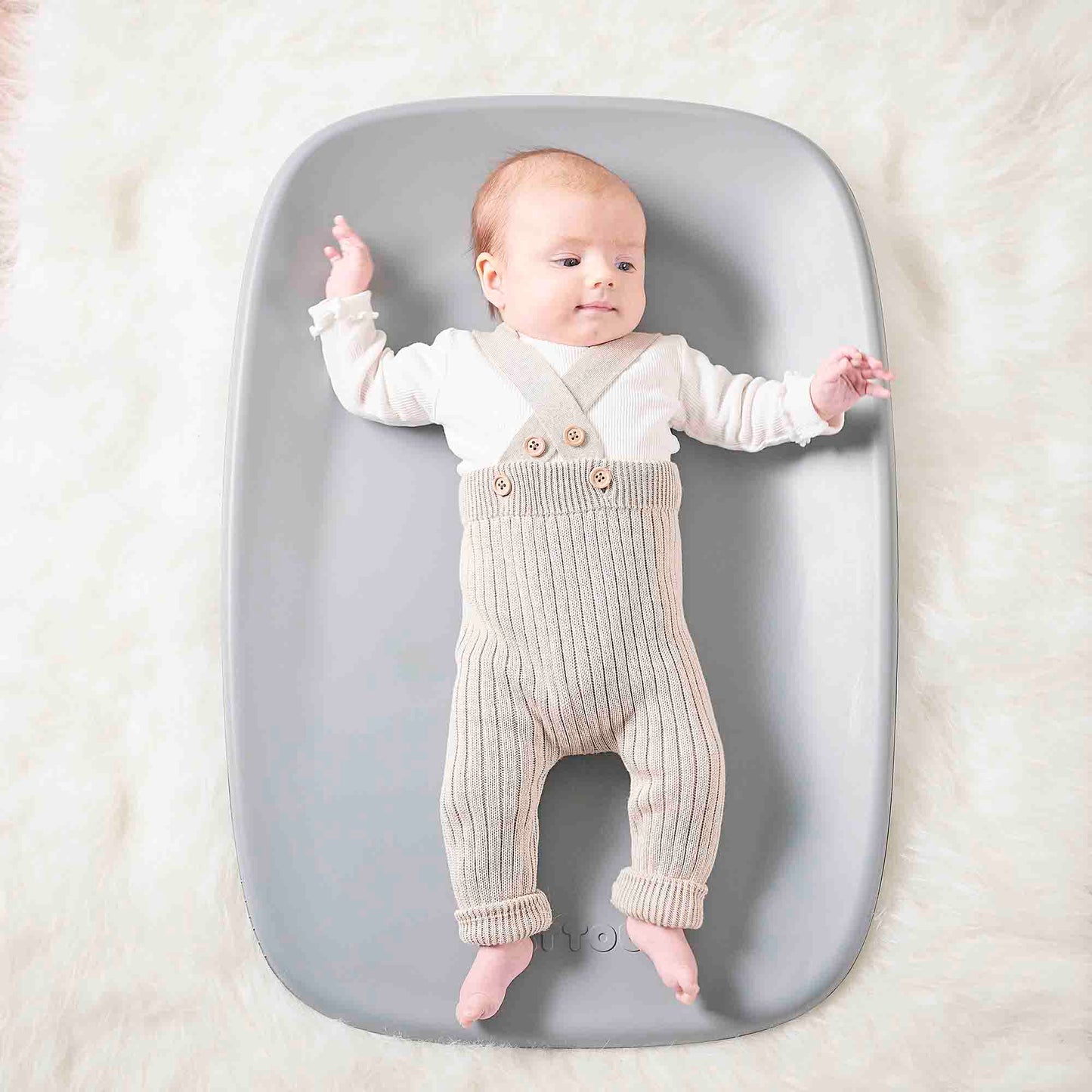 Baby lying on a gray mat with a white background