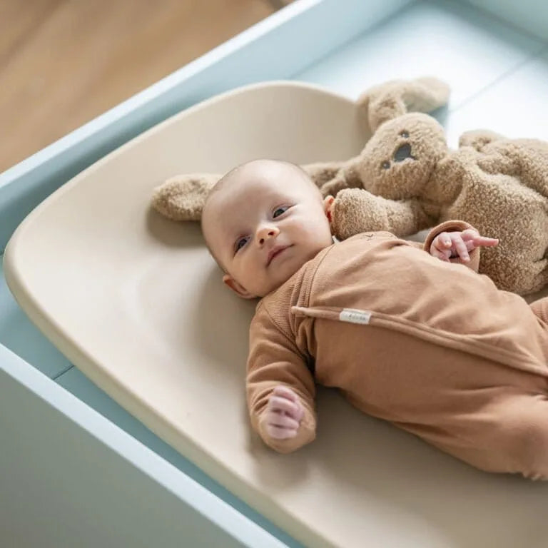 Baby lying on a changing table with a brown teddy bear