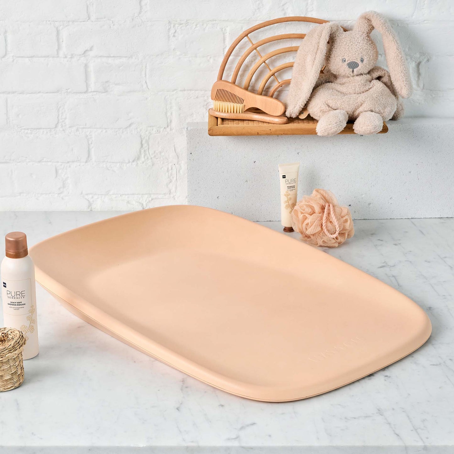 Beige bath mat on a marble surface with baby products and a plush toy in the background.
