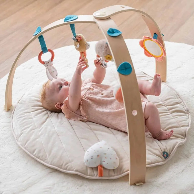Baby playing with a wooden play gym on a soft surface