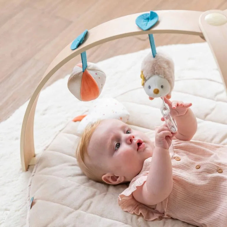Baby lying on a white blanket with a baby gym and hanging toys