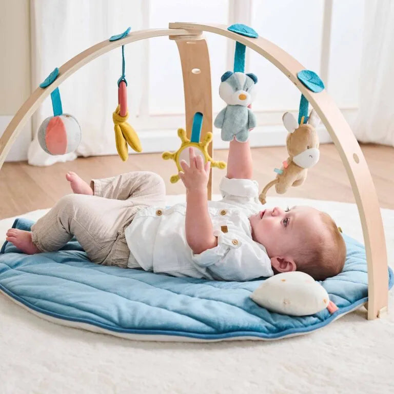 Baby playing with a wooden play gym on a blue mat