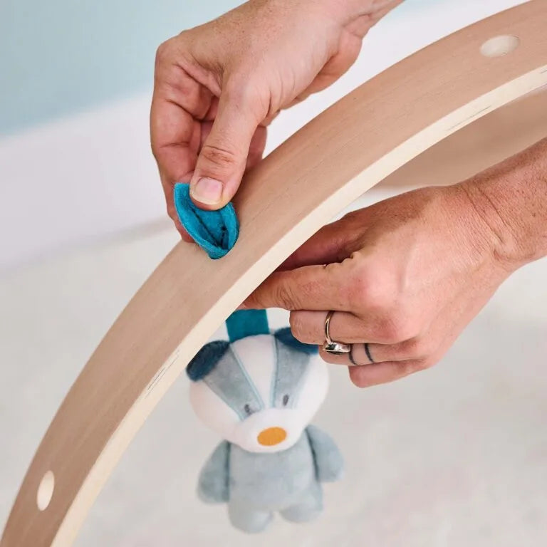 Person attaching a blue plush toy to a wooden ring on a light background