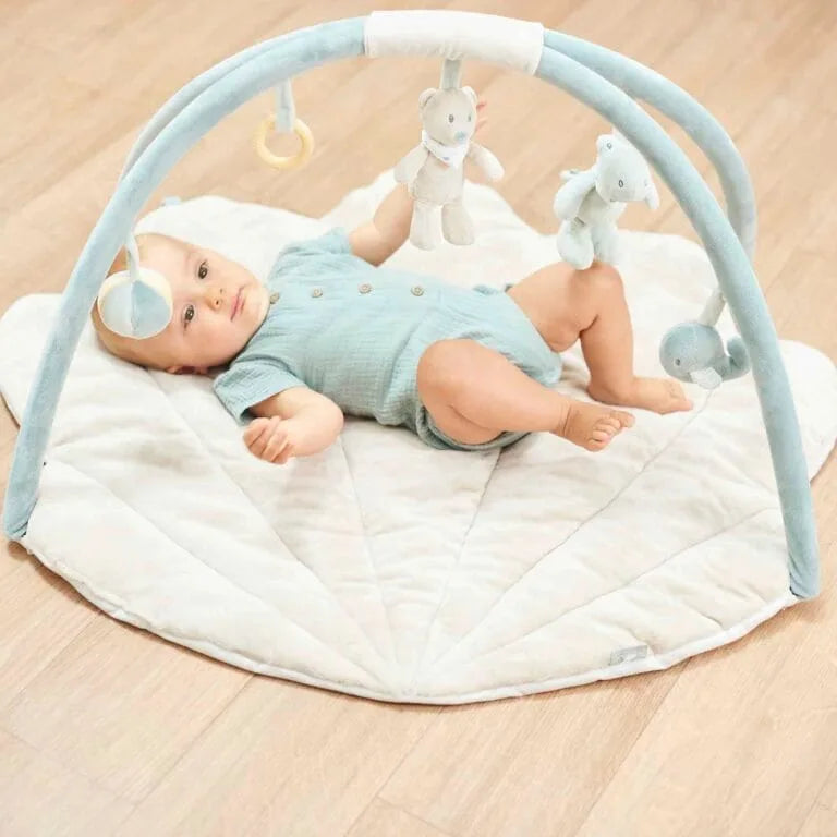 Baby lying on a white mat with a blue play gym