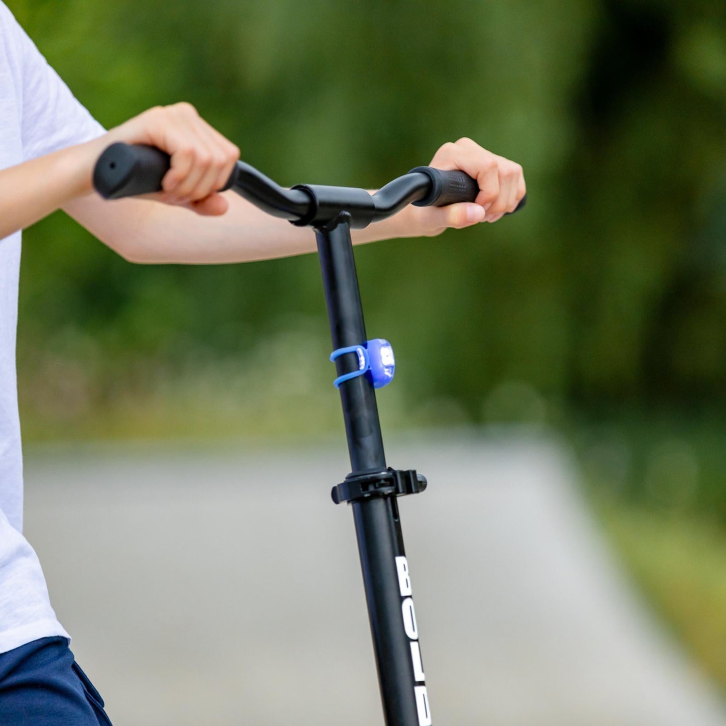 Person holding a black scooter with a blurred green background