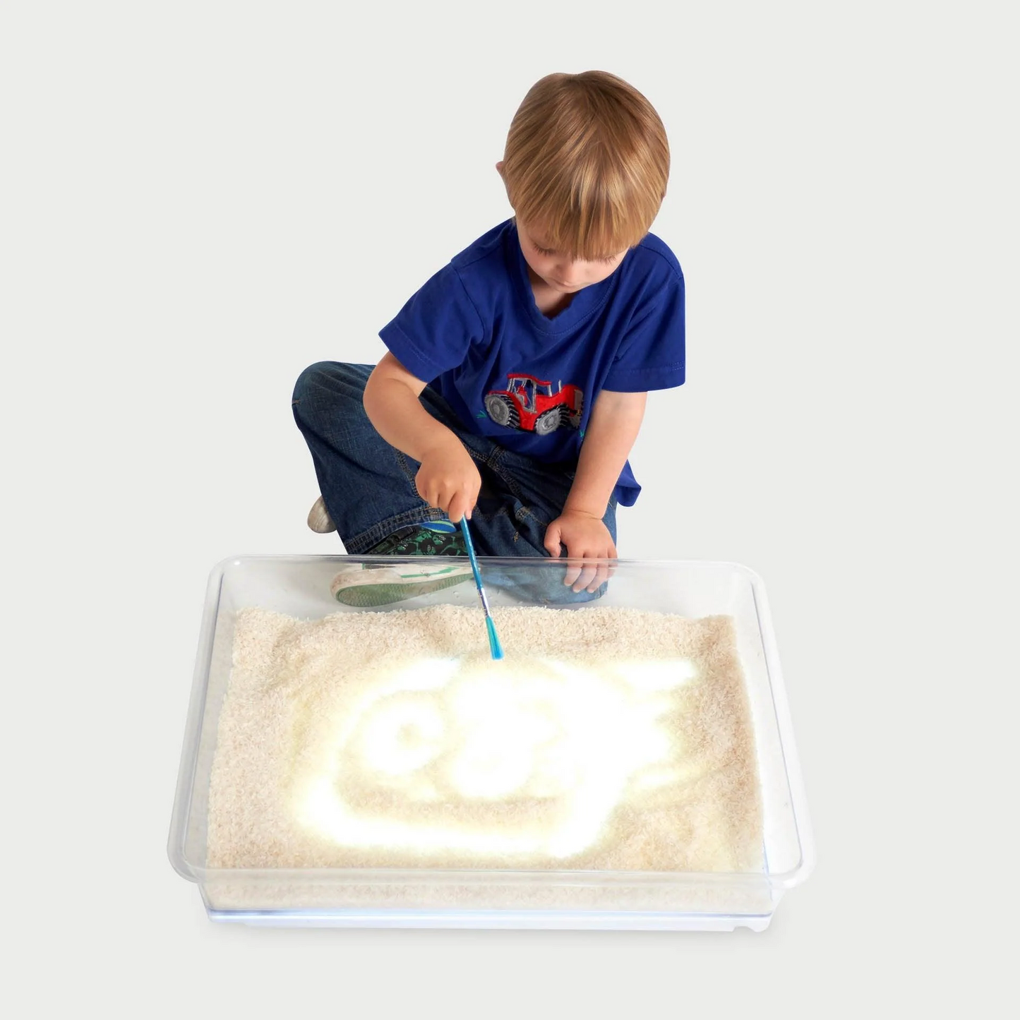 Child playing with rice in a tray over a light panel