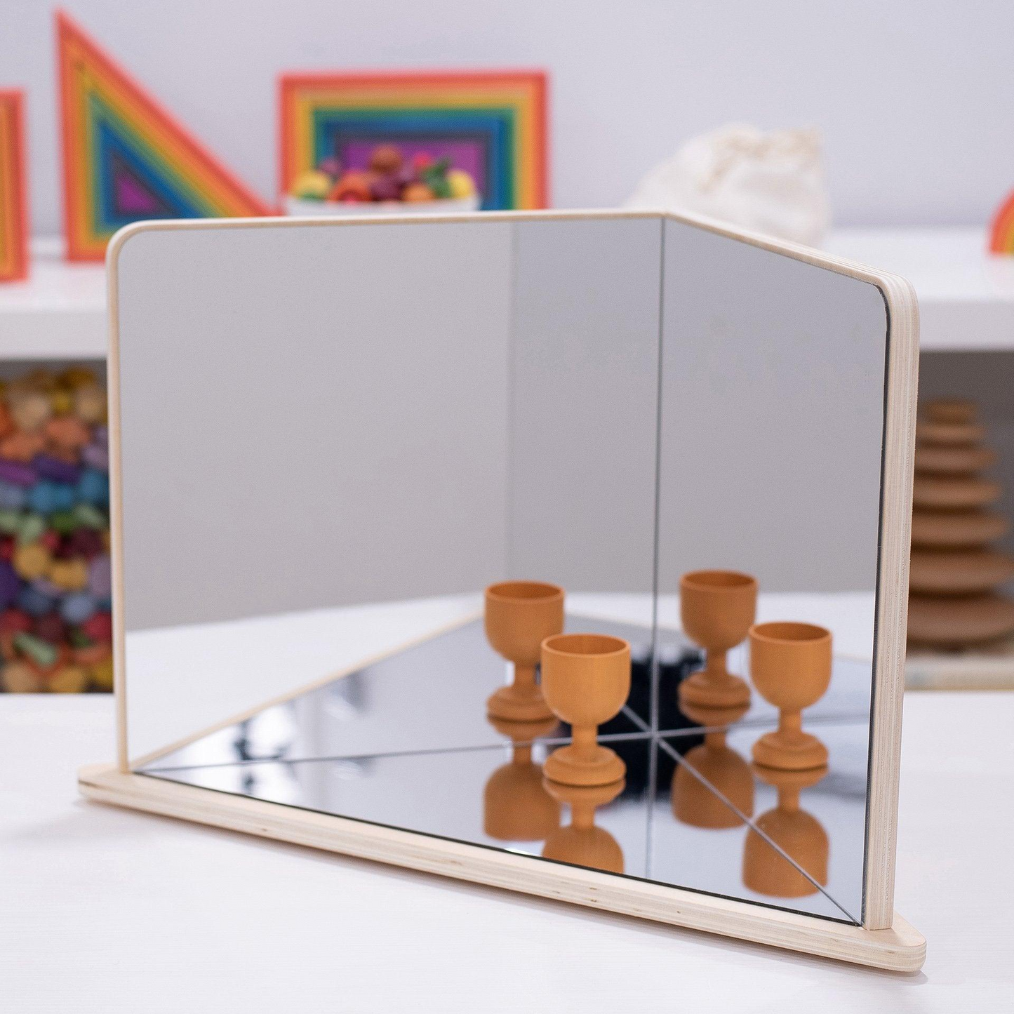 Reflective mirror with wooden cups on a white table, colourful background