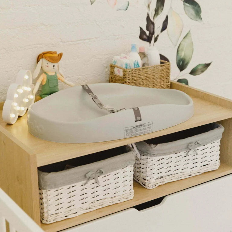 Nursery setup with a changing table, baskets, and toys on a wooden shelf.