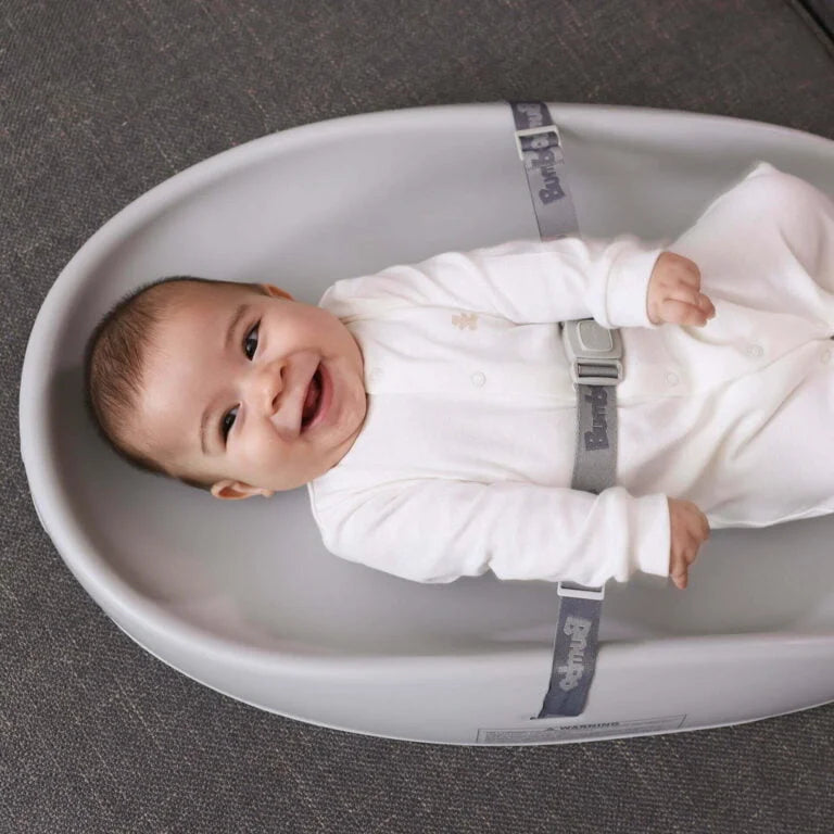 Baby in a white outfit lying on a gray cushion
