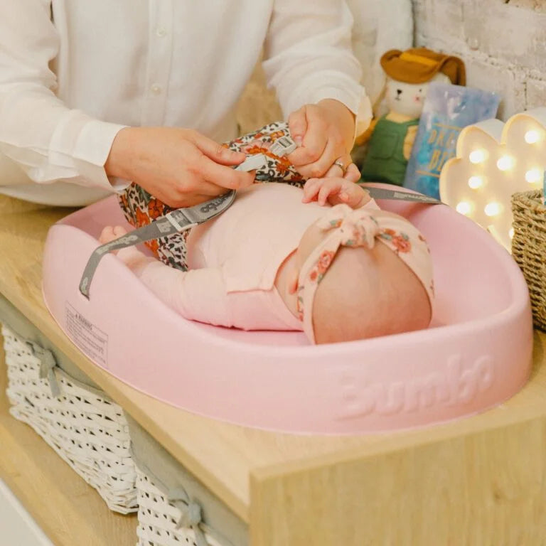 Baby lying on a pink cushion with a person adjusting something near the baby's head.