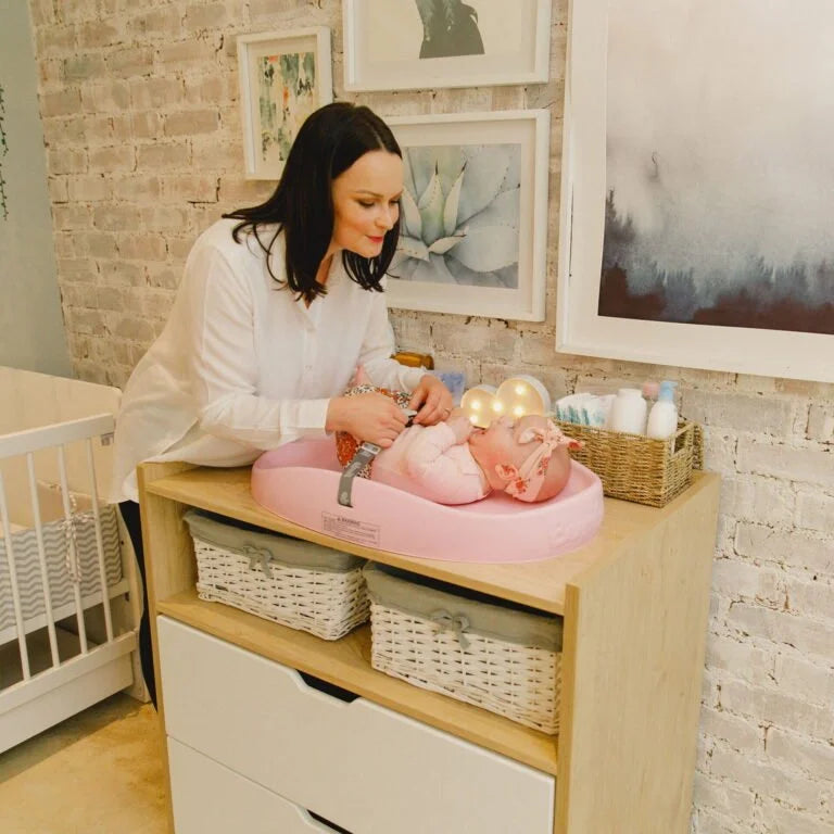 Woman changing a baby on a pink changing table in a nursery.