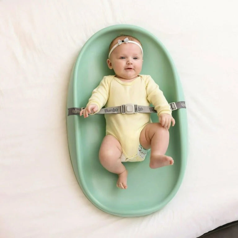 Baby sitting in a green baby seat with a white background