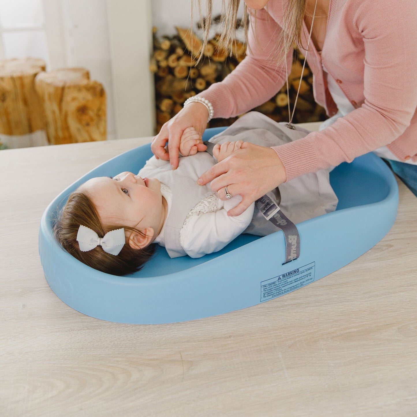 Baby lying on a blue cushion with a woman adjusting it, in a home setting.