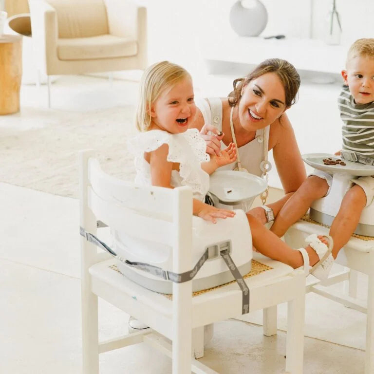 Woman with two children sitting on a white chair in a bright room.