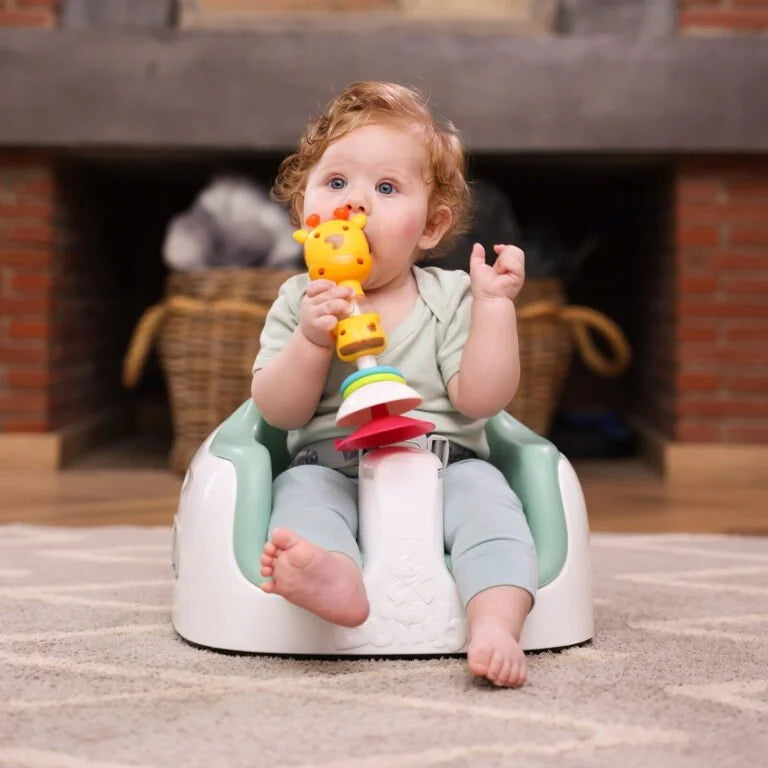 Child sitting on a baby seat with a colorful toy, indoors.