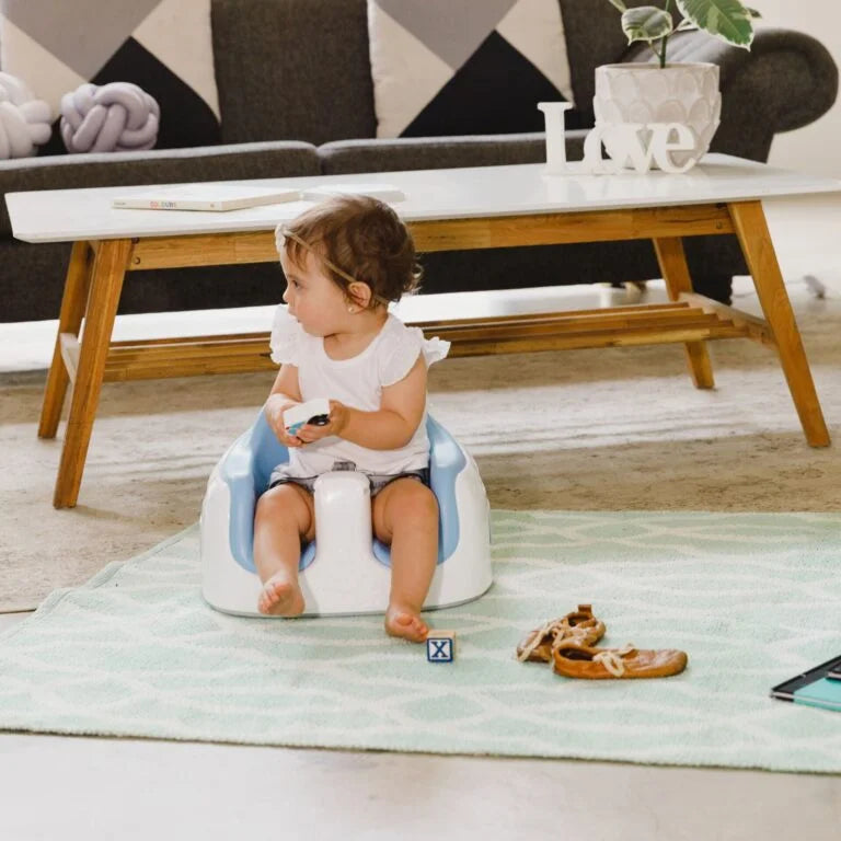 Child sitting on a blue and white potty chair in a living room.