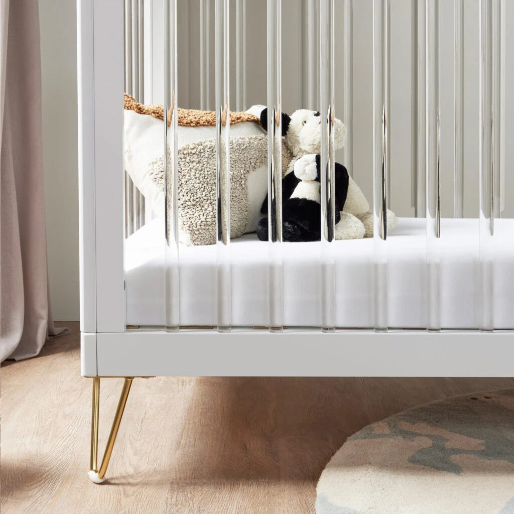 White crib with stuffed animals inside, placed against a neutral wall.