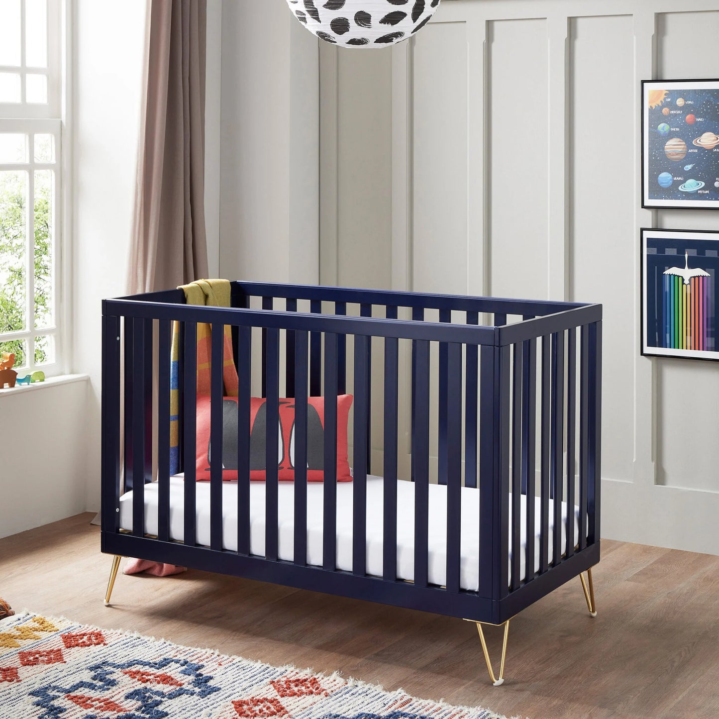 Navy crib with gold legs in a nursery setting with colorful decor