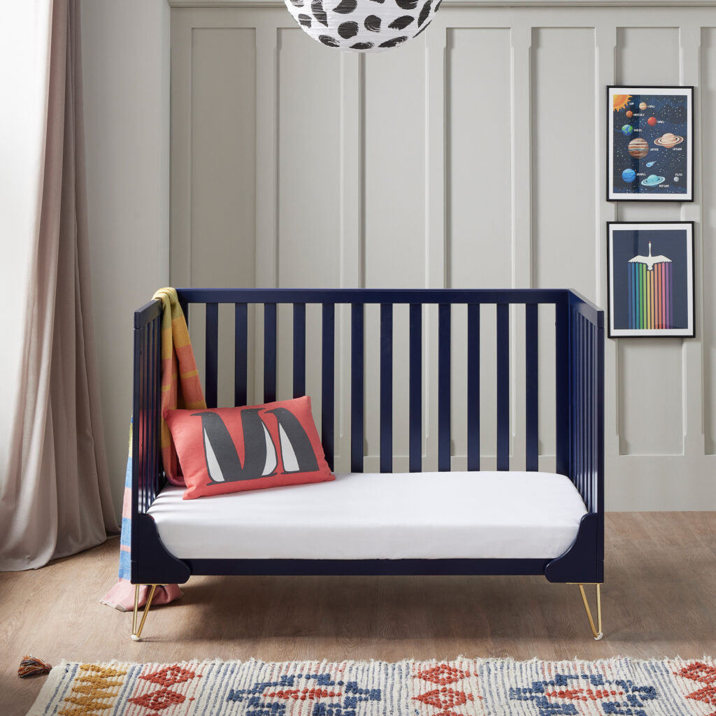 Navy crib with white mattress in a room with framed artwork on the wall.