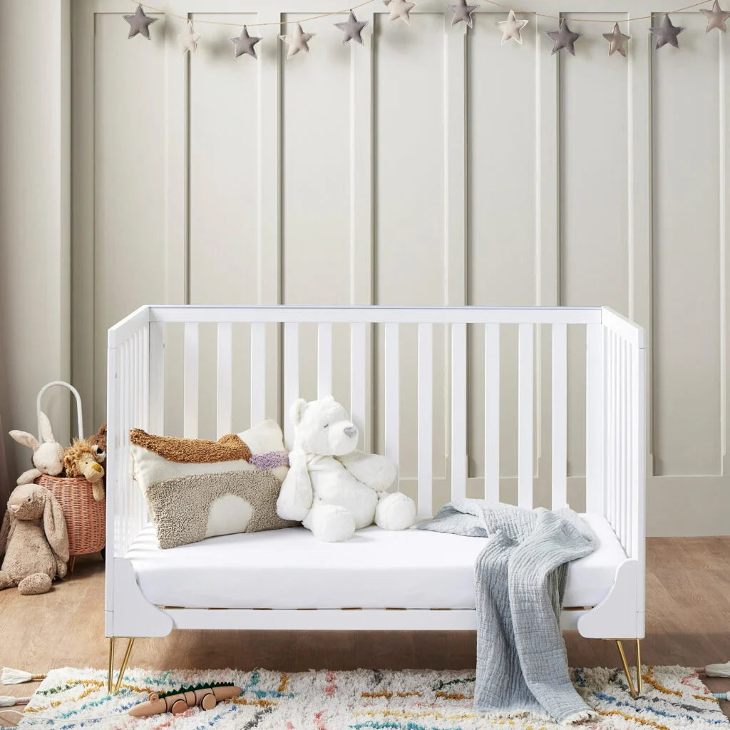 White crib with toys in a nursery setting with star decorations on the wall.