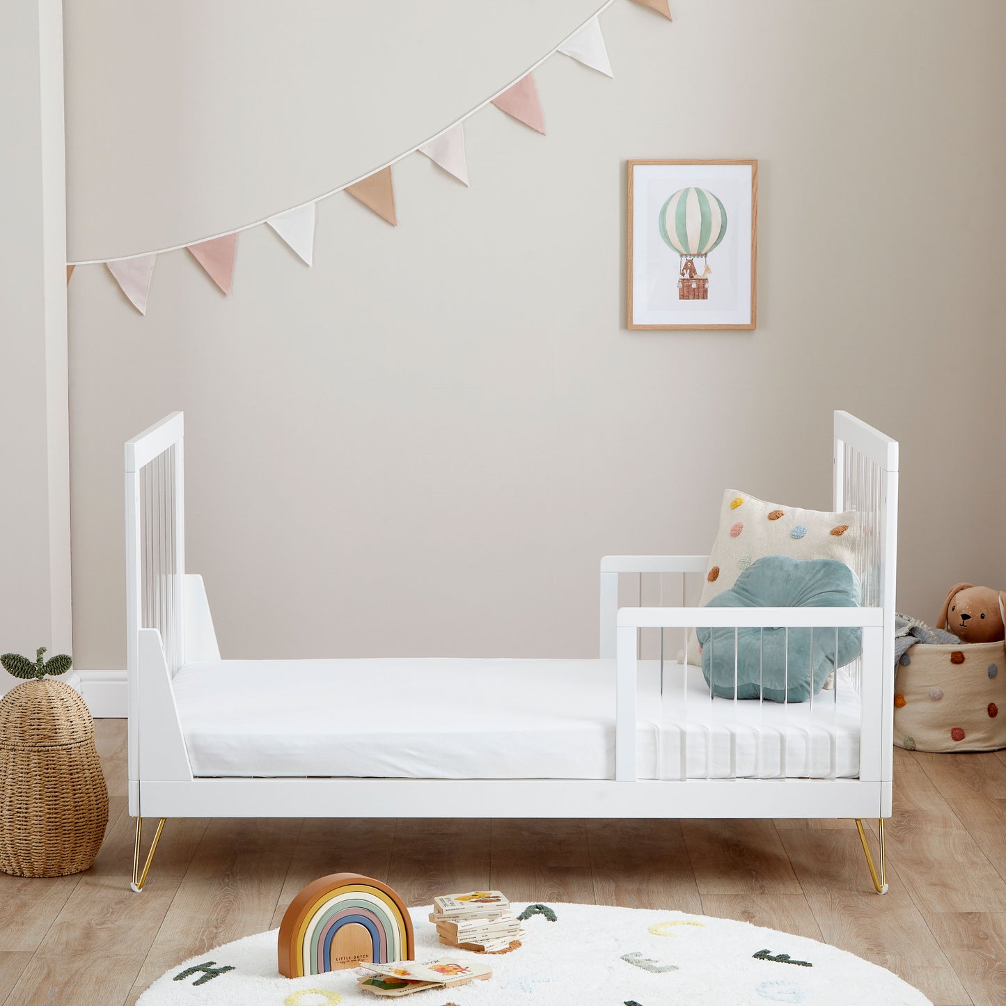 Kimi Cot Bed in toddler style with a Acrylic spindles in a bedroom with rug and toys.