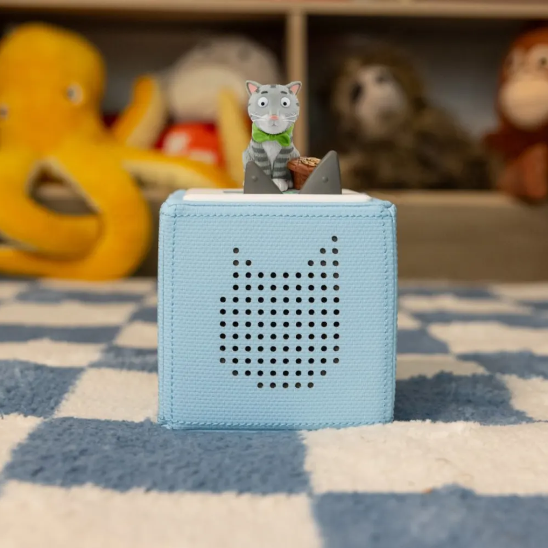 Blue toy box with a cat figurine on top, surrounded by plush toys on a checkered blanket.