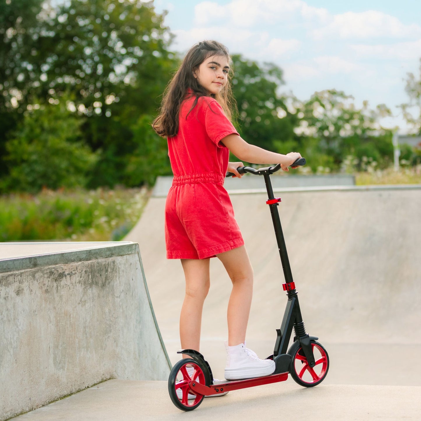 Girl in a red dress standing next to a scooter in an outdoor setting