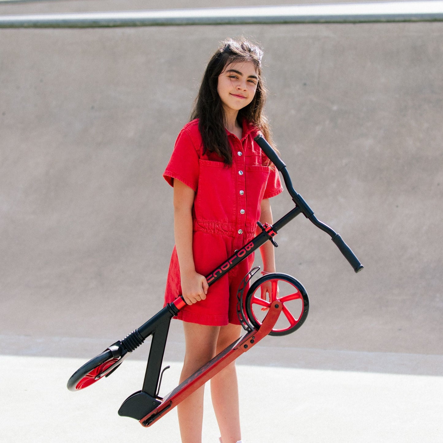 Girl in a red dress holding a red scooter against a plain background