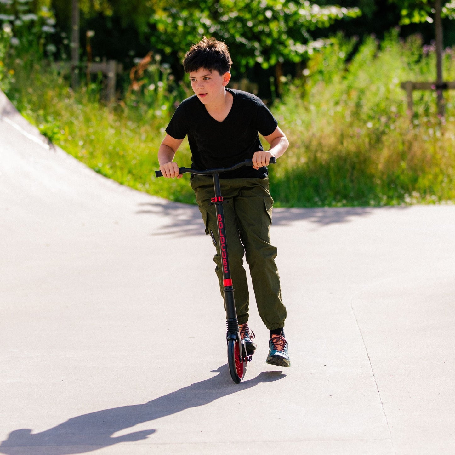 Child riding a scooter on a paved path with greenery in the background
