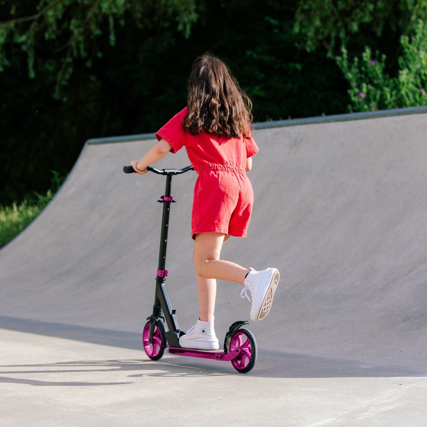 Child riding a scooter on a concrete surface with greenery in the background